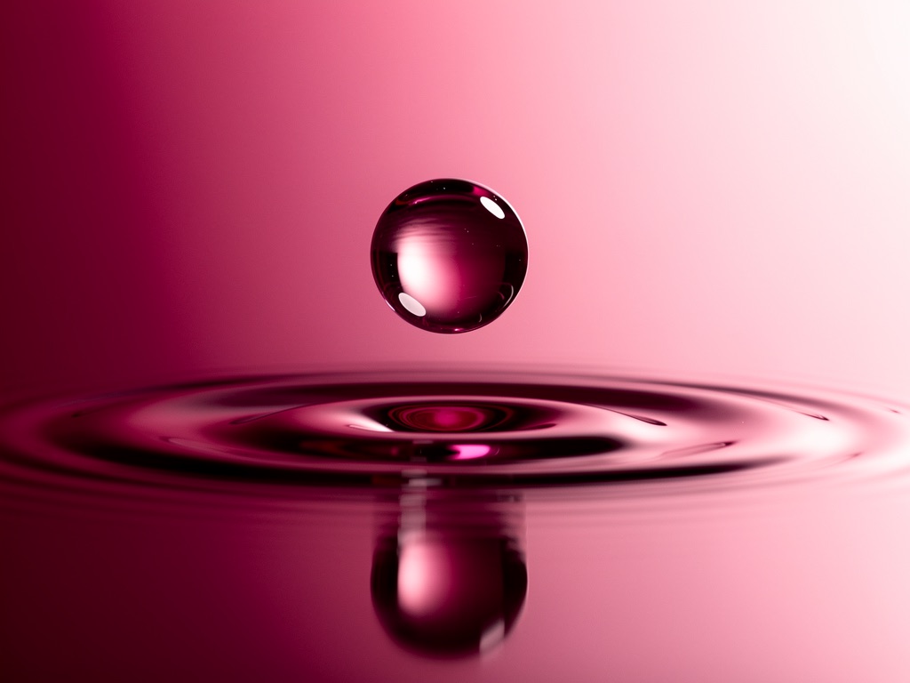 A vivid magenta liquid drop above soft ripples