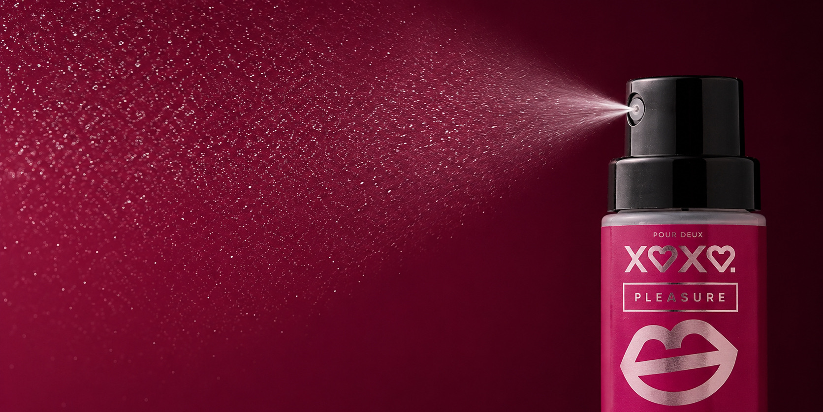 Pleasure bottle releasing a fine mist against deep raspberry